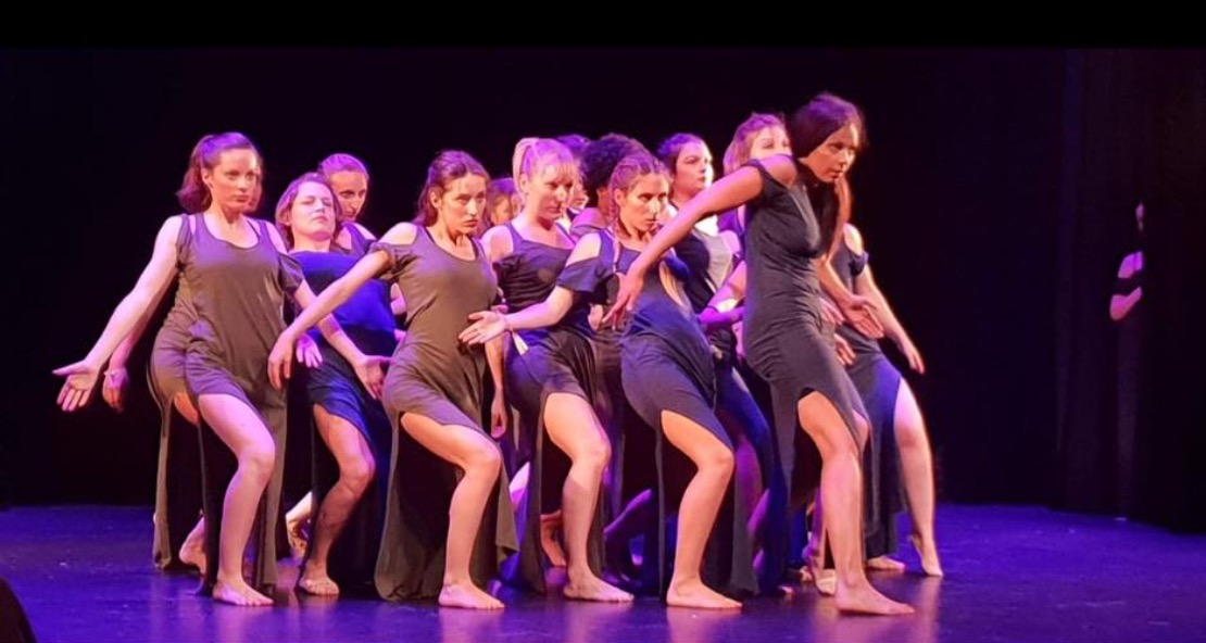 Élèves adultes de Mishell en spectacle, chorégraphie en robes sombres sous une lumière violette