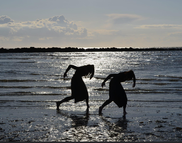 Deux danseuses en silhouette au bord de l'eau au coucher du soleil
