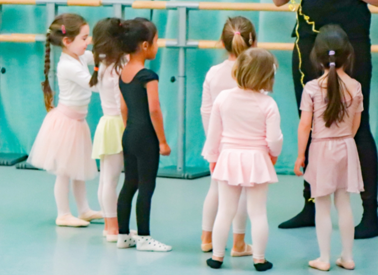 Groupe d'enfants en cours d'éveil à la danse devant la barre du studio